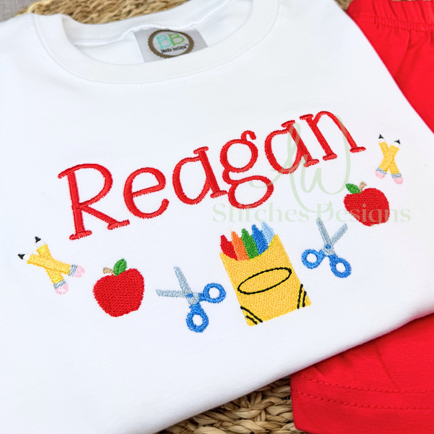 White shirt with 'Reagan' and school supplies embroidery on a red background