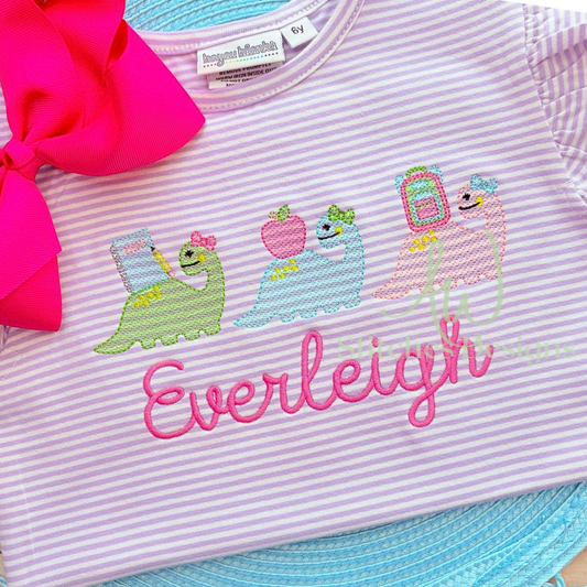 Children's shirt with embroidered designs and 'Everleigh' text, featuring a pink bow and blue trim.