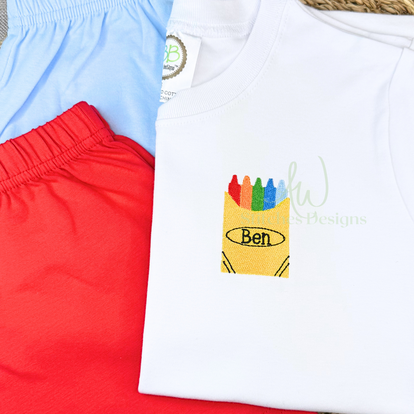 White shirt with colorful crayon design and 'Ben' text, paired with red shorts and blue pants.