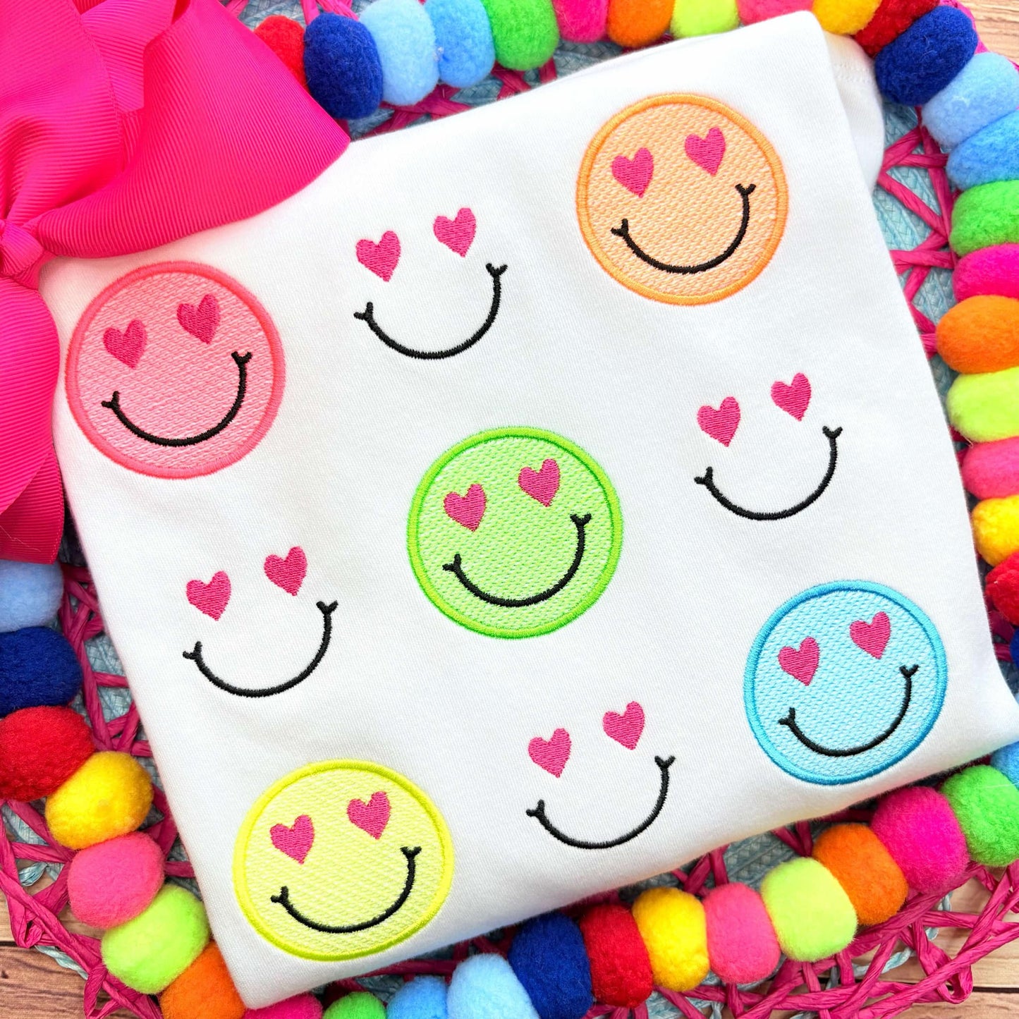 White fabric with colorful smiley face patches on a multicolored pom-pom background