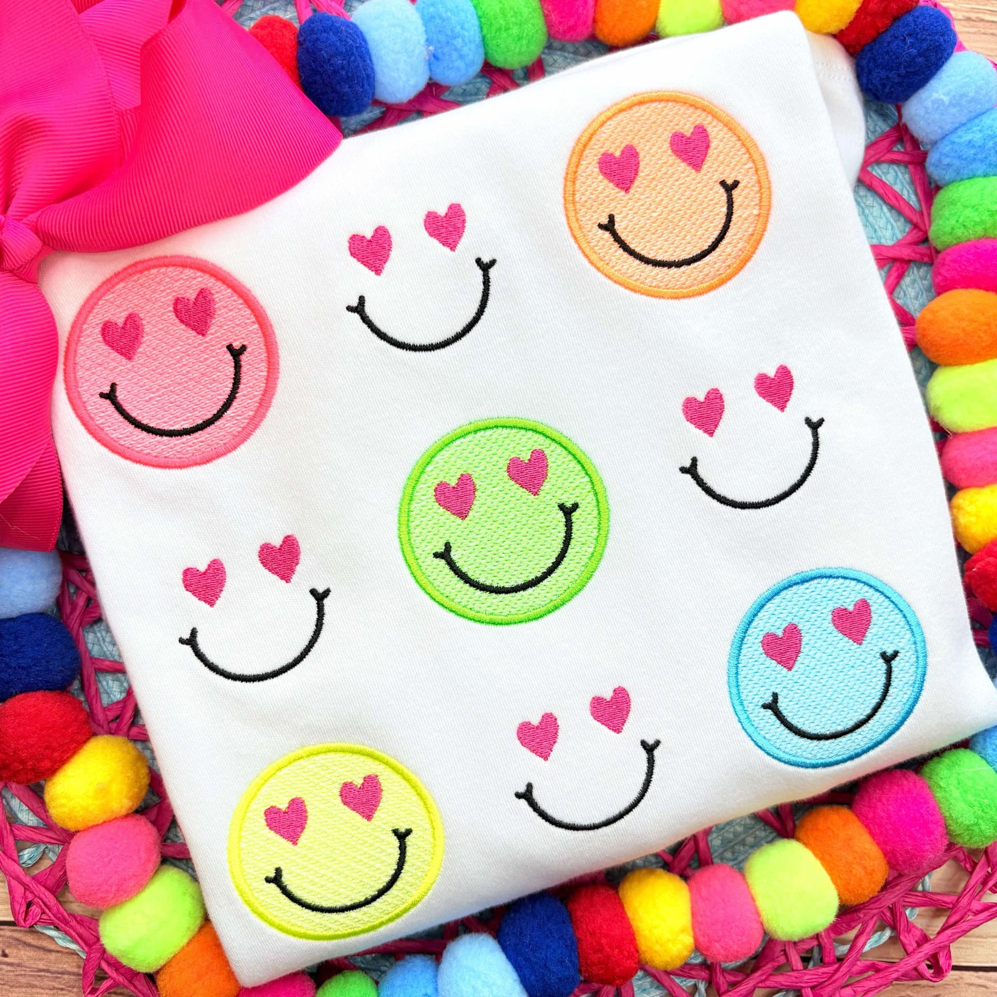 White fabric with colorful smiley face patches on a multicolored pom-pom background