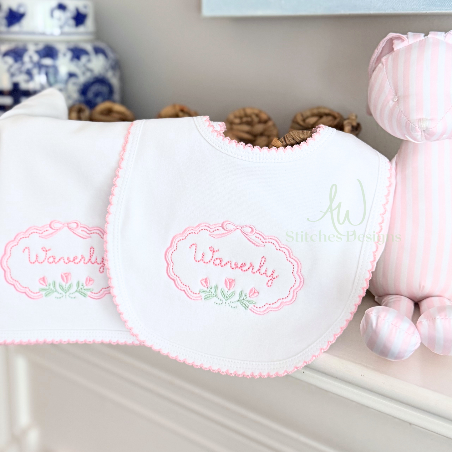 White bib with pink embroidery on a shelf with decorative items