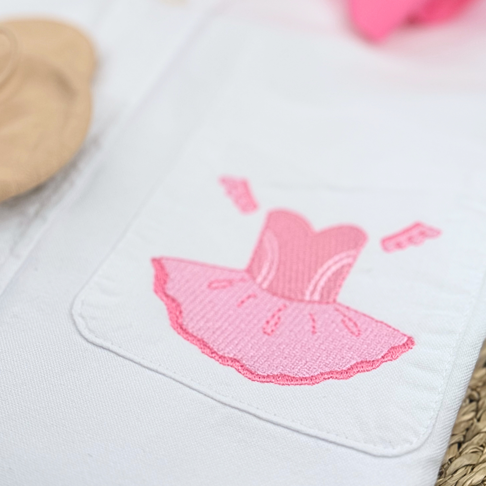 White fabric with pink embroidered dress design on a light background