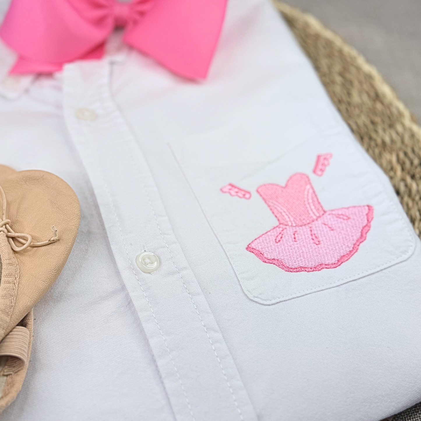 White shirt with pink embroidered dress design and pink bow on a neutral background