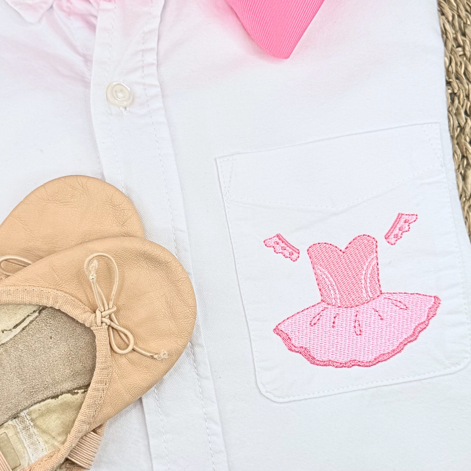 White shirt with pink embroidered ballet skirt design and beige ballet shoes on a white background