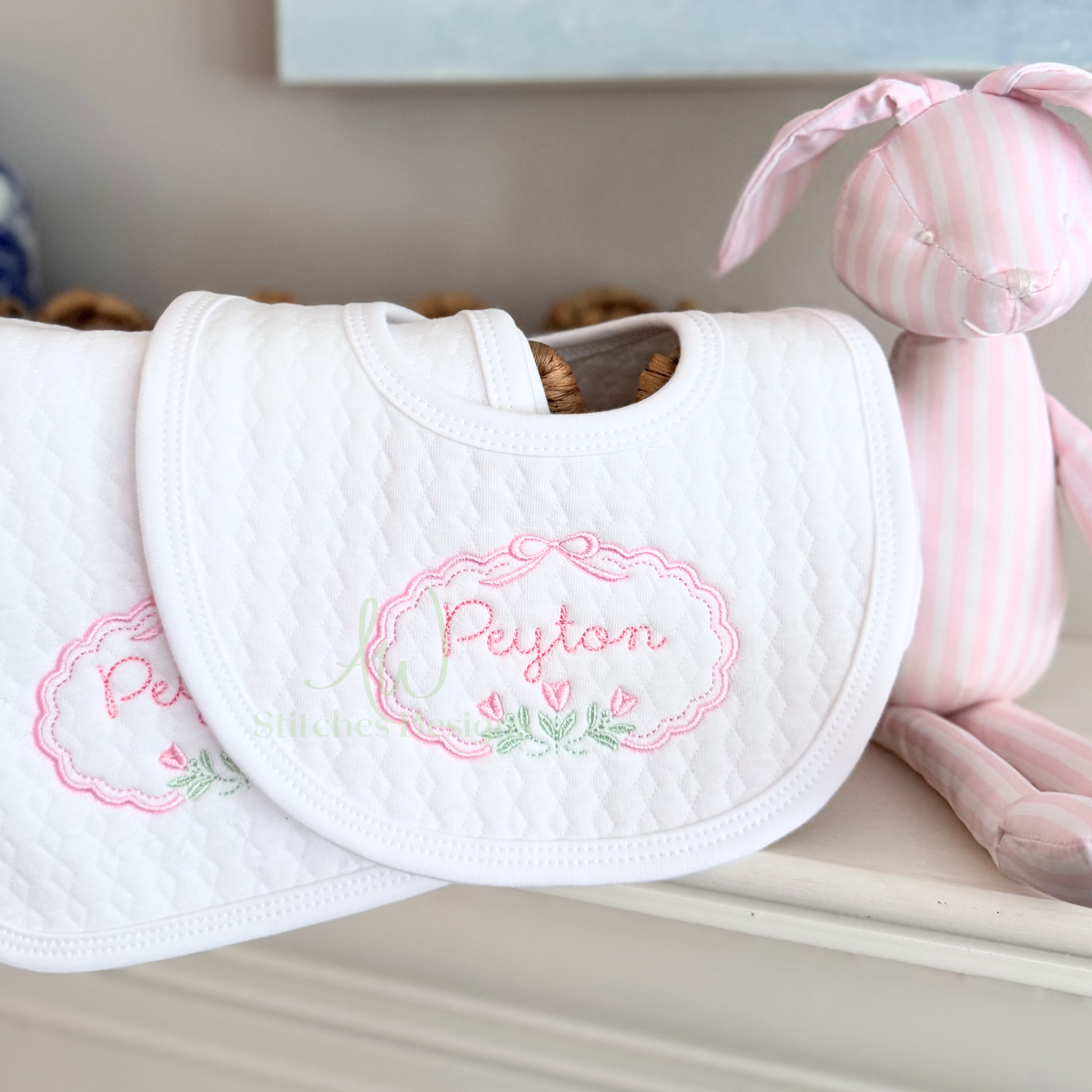 White bib with embroidered name 'Peyton' on a shelf with a pink toy.
