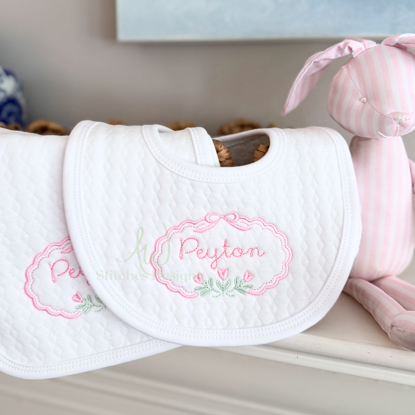 White bib with embroidered name 'Peyton' on a light surface with pink plush toy.