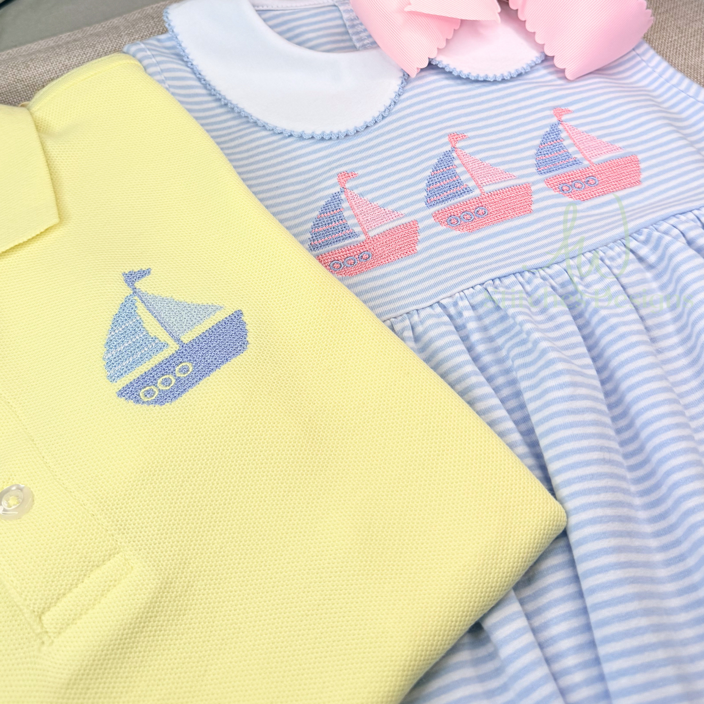 Yellow baby outfit with sailboat design and blue striped dress with pink sailboats on a textured surface.