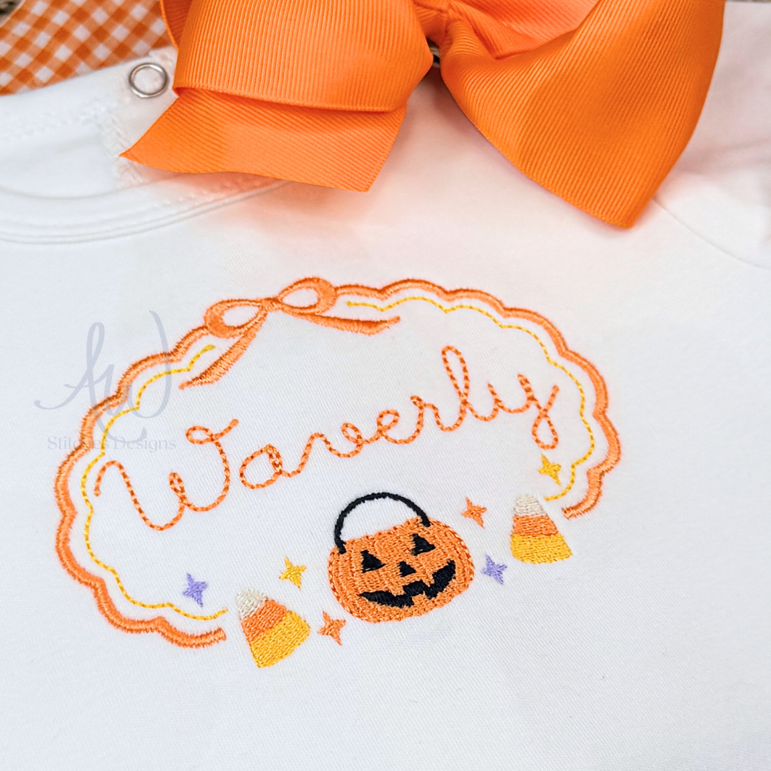 Close-up of a white baby bodysuit or onesie with an orange embroidered Halloween design reading 'Waverly,' featuring a jack-o'-lantern, candy corn, stars, and an orange ribbon motif. A large orange bow is partially visible at the top.
