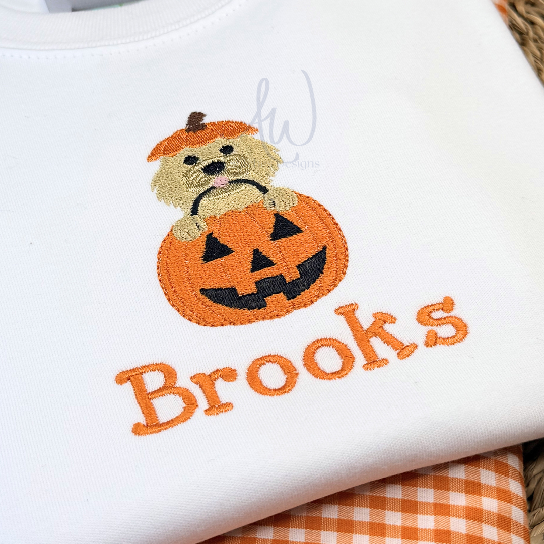 Embroidered design of a dog in a pumpkin with 'Brooks' text on a white fabric background.