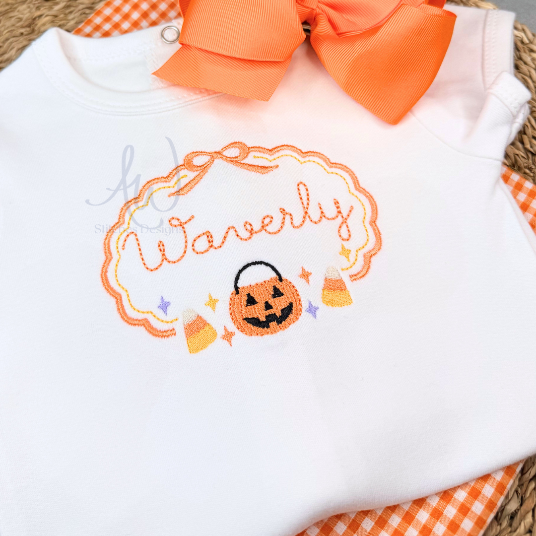White baby bodysuit with an orange and black embroidered Halloween design featuring the name 'Waverly' in script, a jack-o'-lantern, candy corn, and stars, styled with an orange bow and orange-and-white gingham fabric.