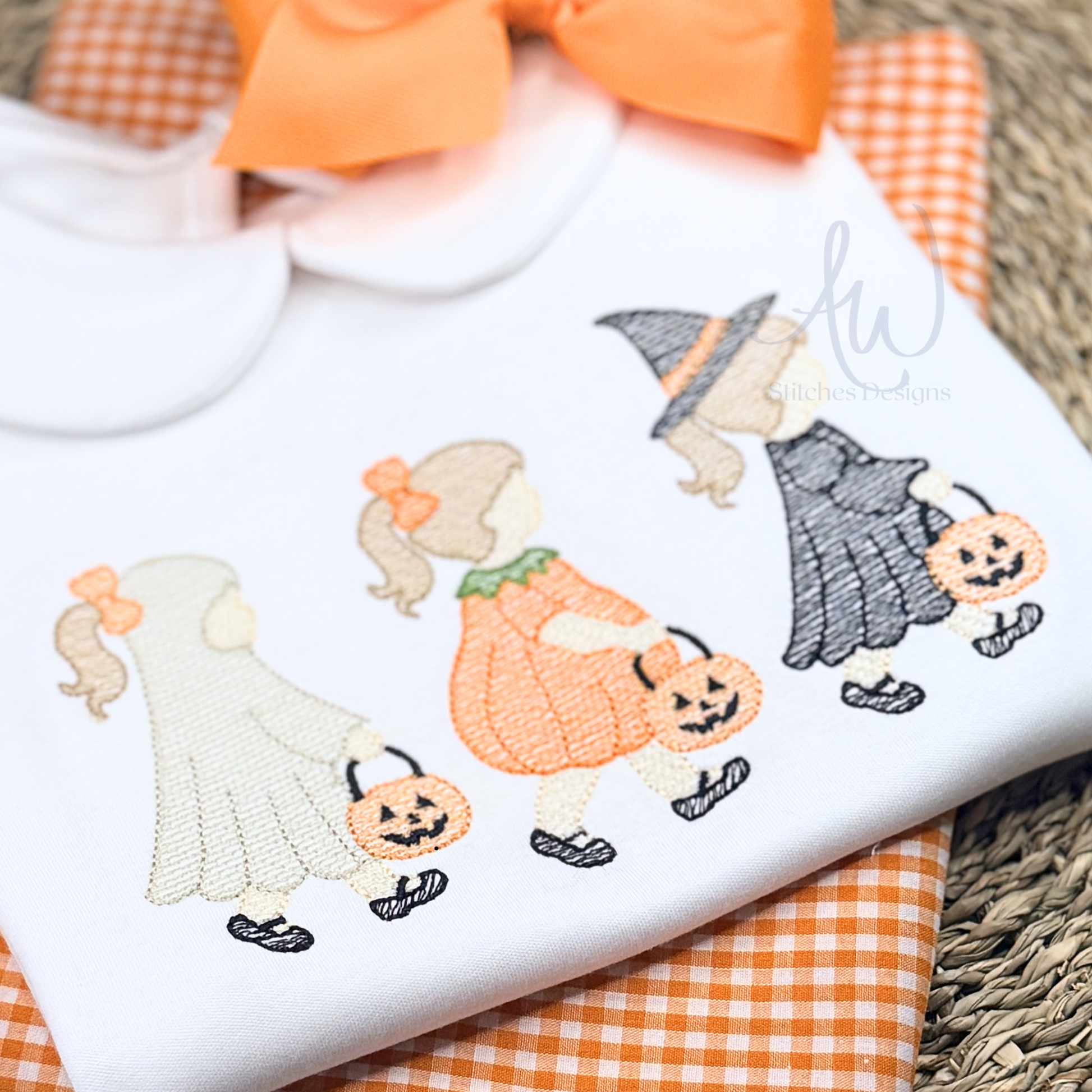 Embroidered design of Halloween-themed characters on a white fabric with orange checkered cloth underneath.