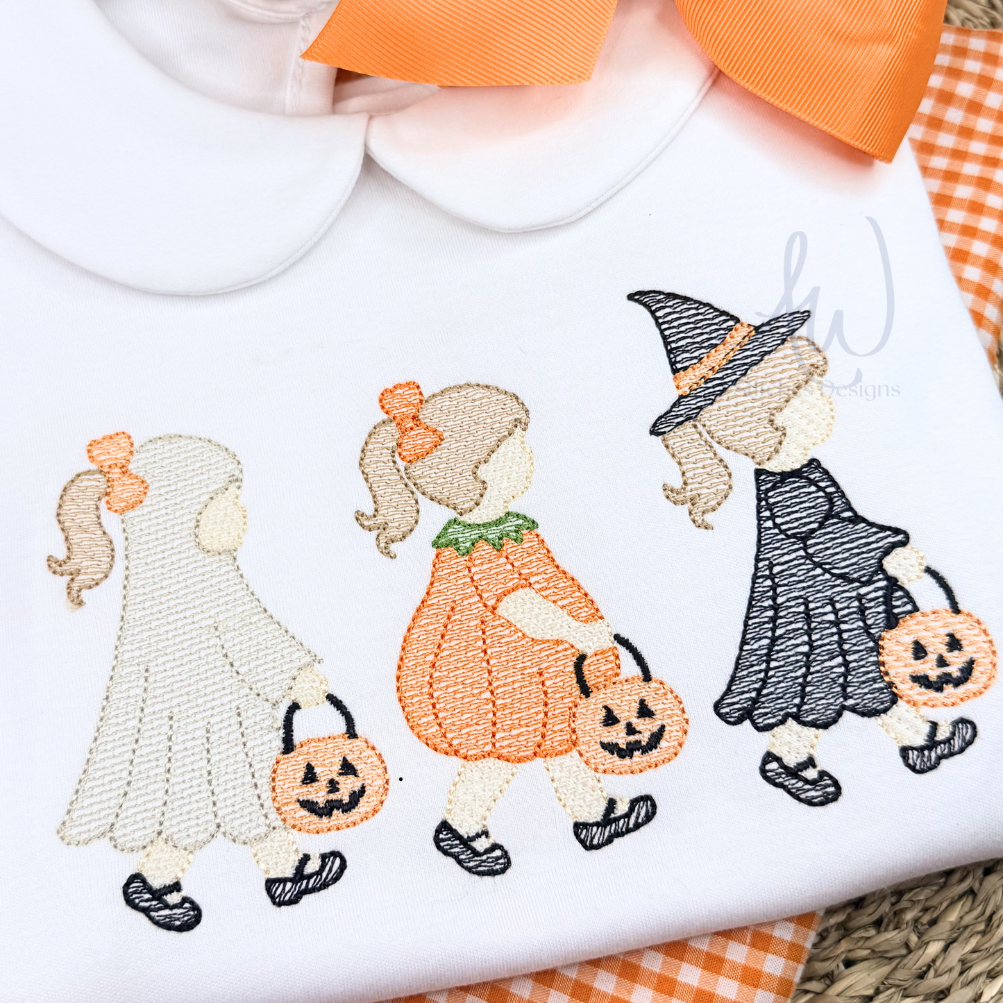 Embroidered design of Halloween-themed characters on a white shirt with orange accents.