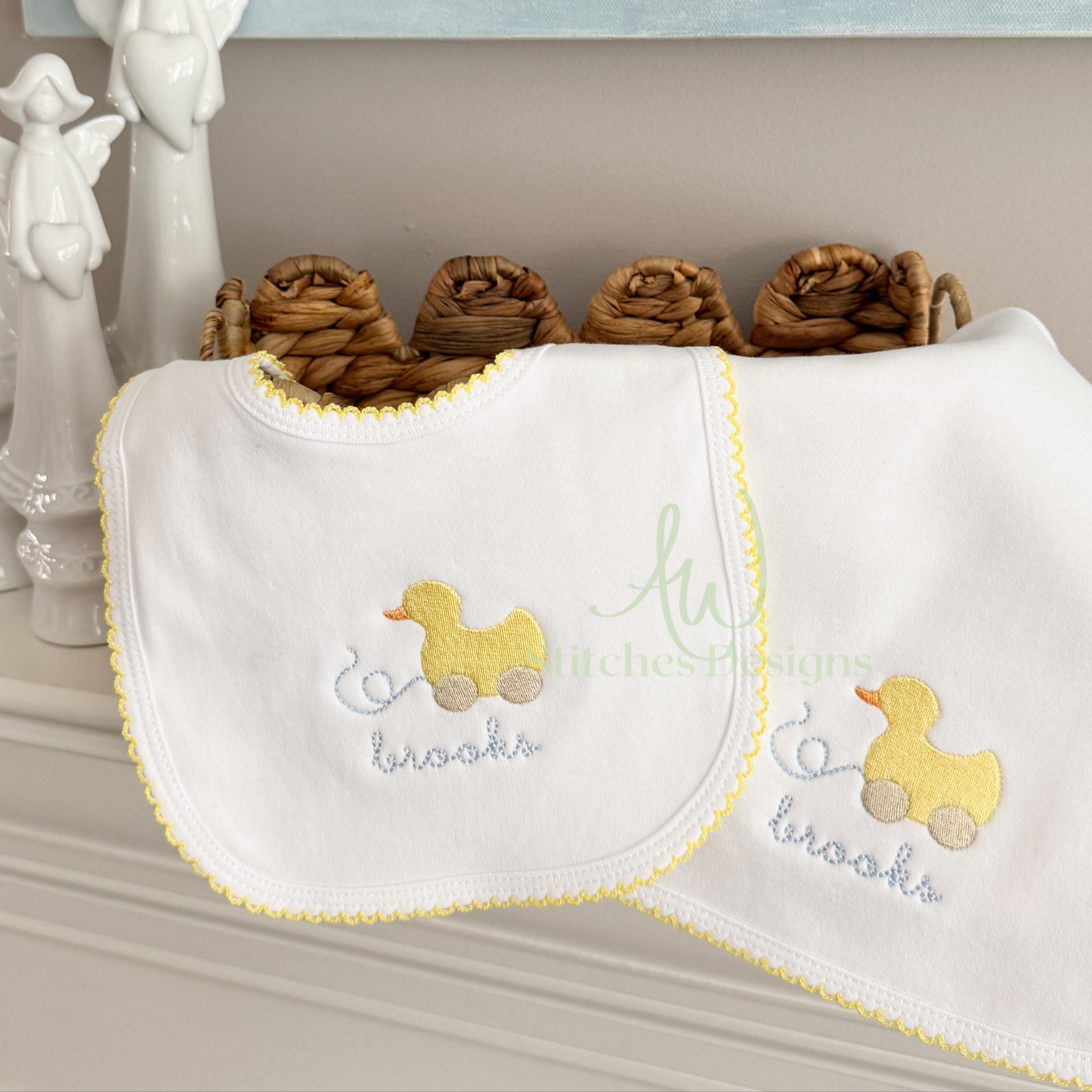 Baby bib with embroidered ducks and text on a shelf with decorative items