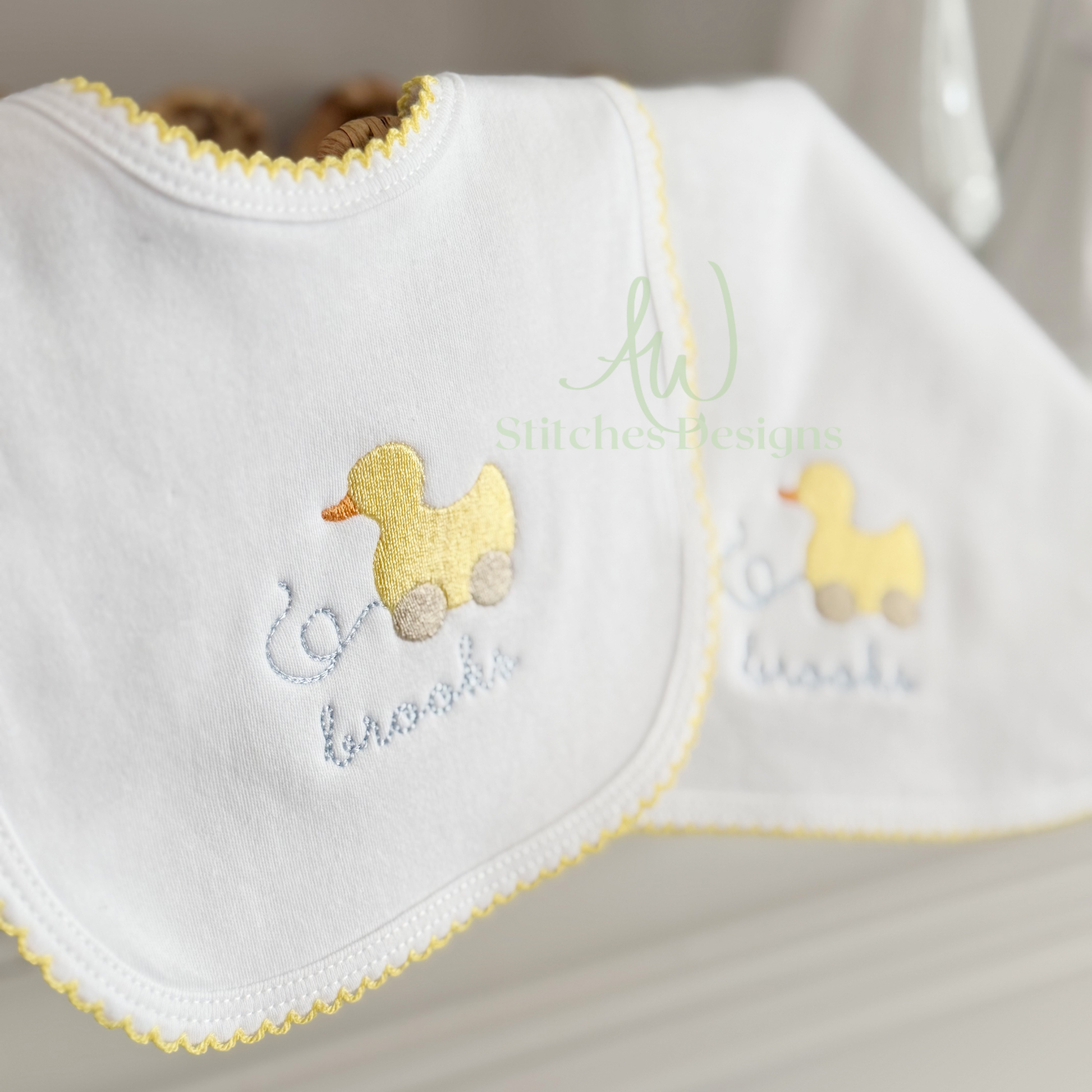 White baby bib with embroidered yellow duck design and text on a neutral background
