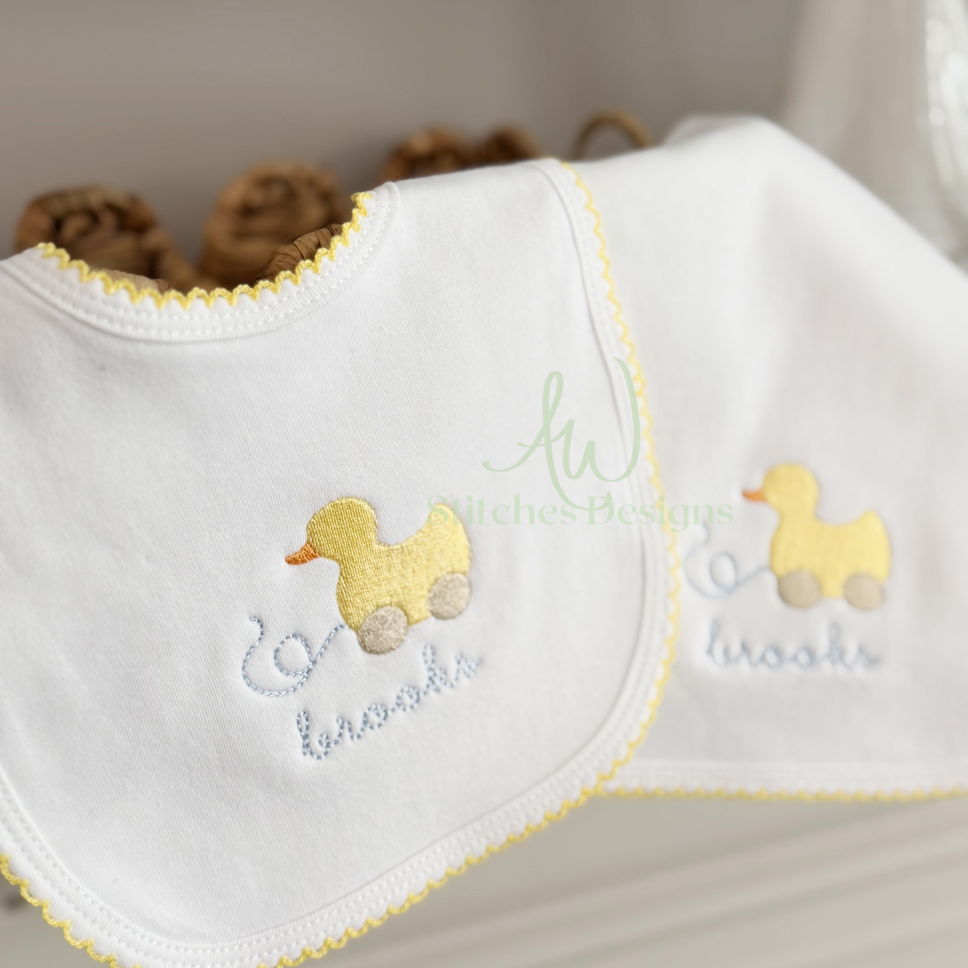 White baby bib with yellow duck embroidery on a neutral background