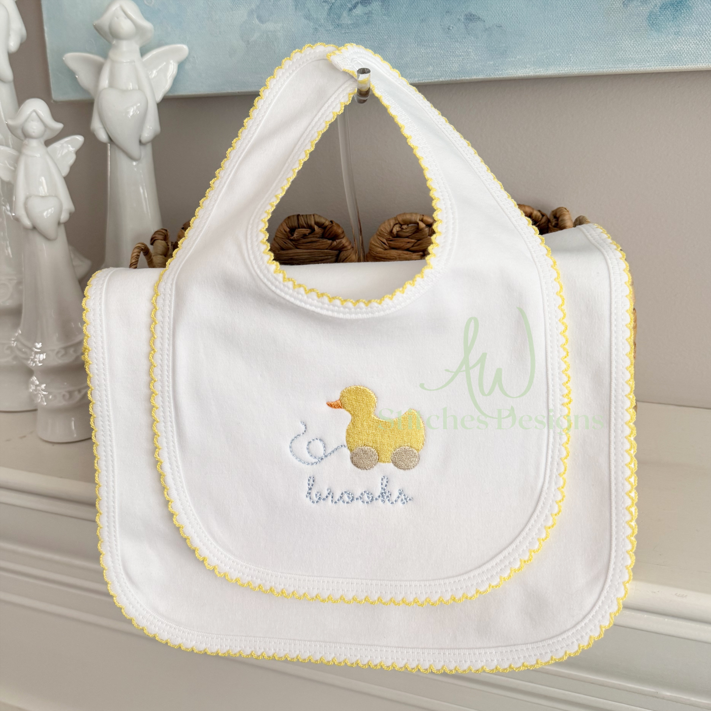 White baby bib with yellow trim and embroidered duck design on a shelf.