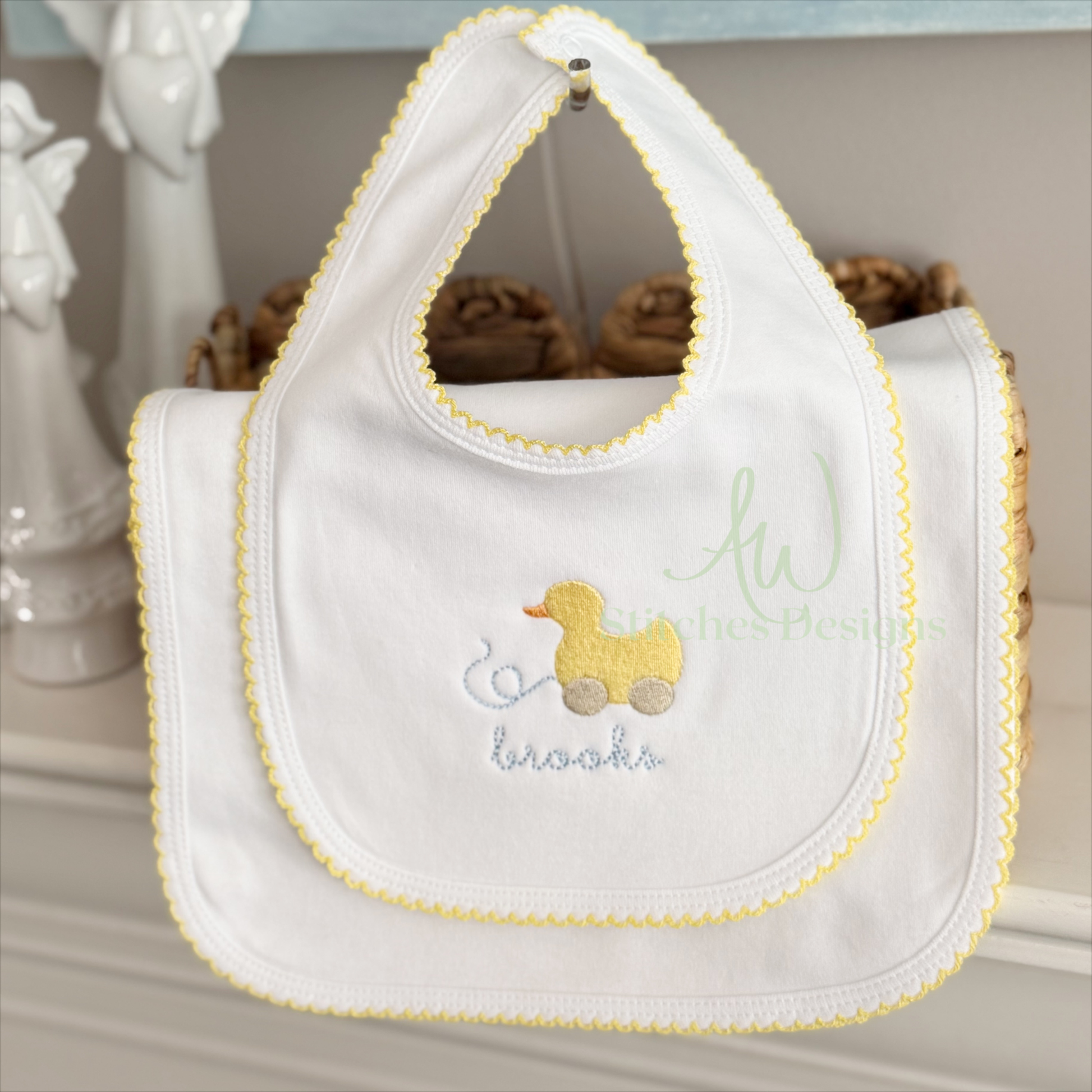 White bib with yellow trim and embroidered duck design on a neutral background