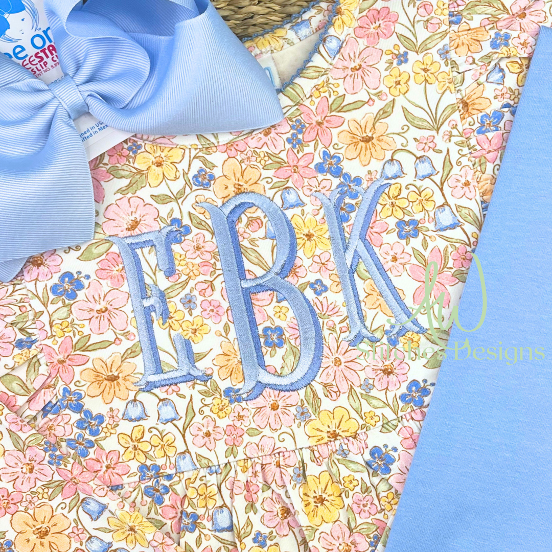 Shadow fishtail monogram satin stitch embroidery font stitched in blue on a floral dress with bow, machine embroidery design file with BX by AW Stitches Designs