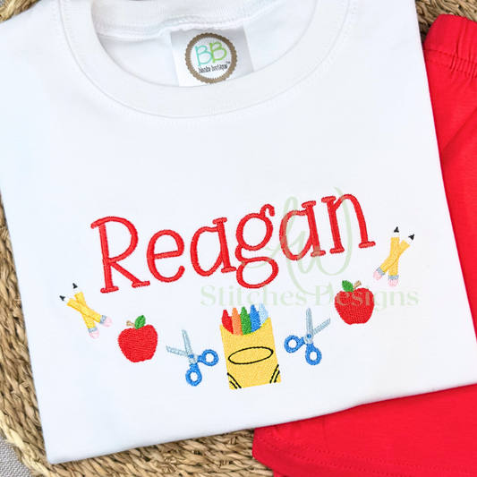 White shirt with 'Reagan' embroidered on it, surrounded by red fabric and a woven mat.