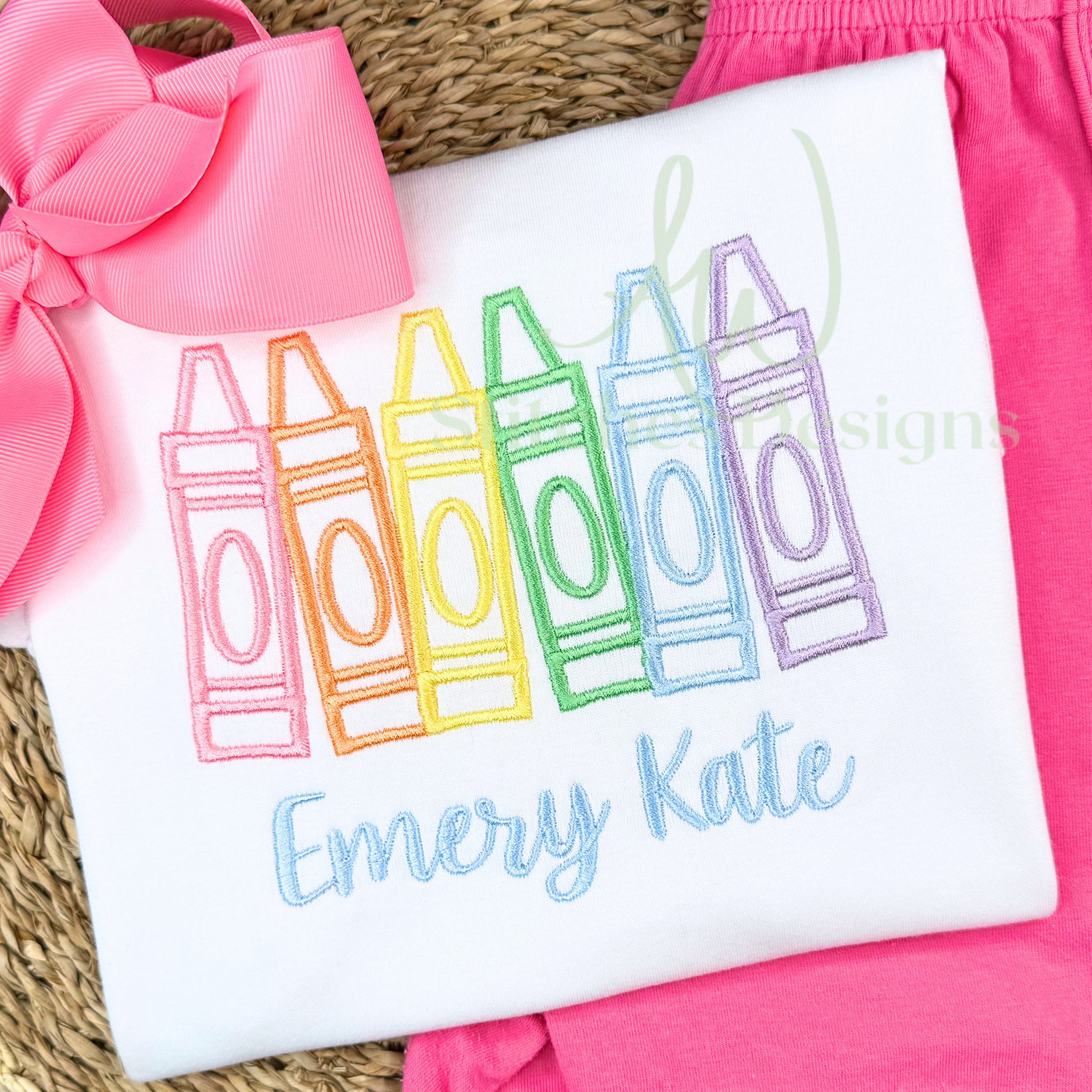 Embroidered shirt with colorful crayon design and 'Emery Kate' text on a pink background.