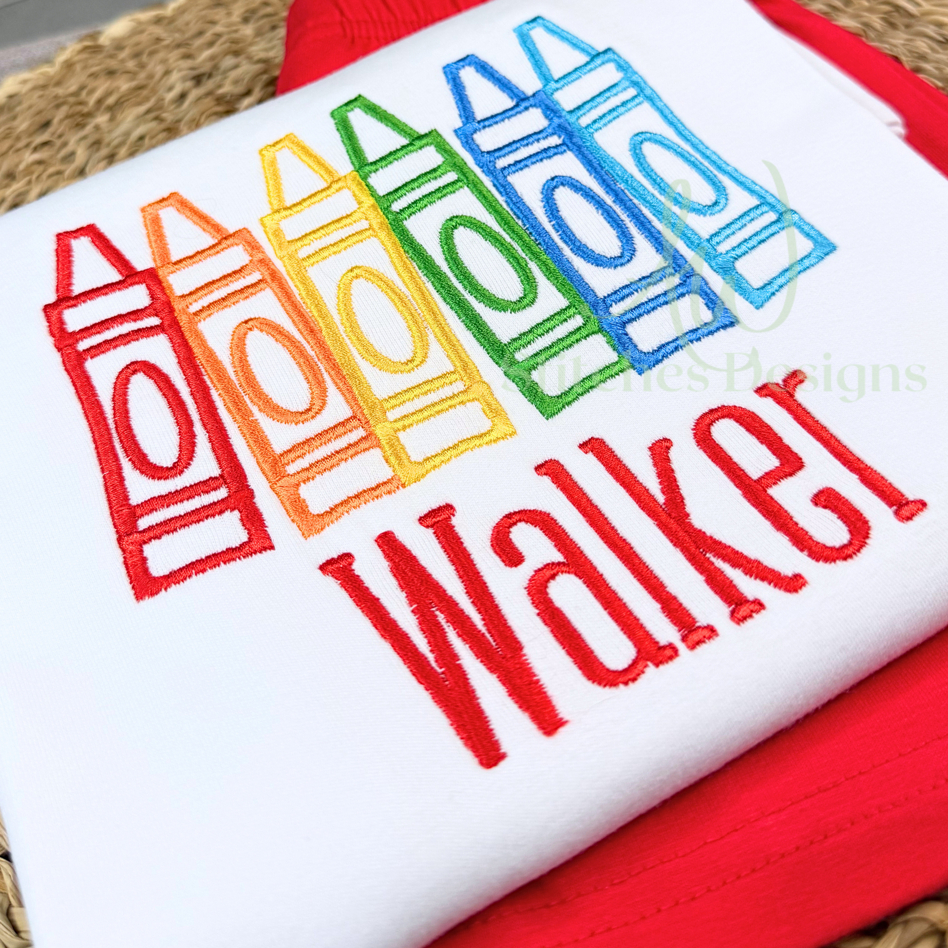 Embroidered design of colorful crayons with the name 'Walker' on a white fabric background.