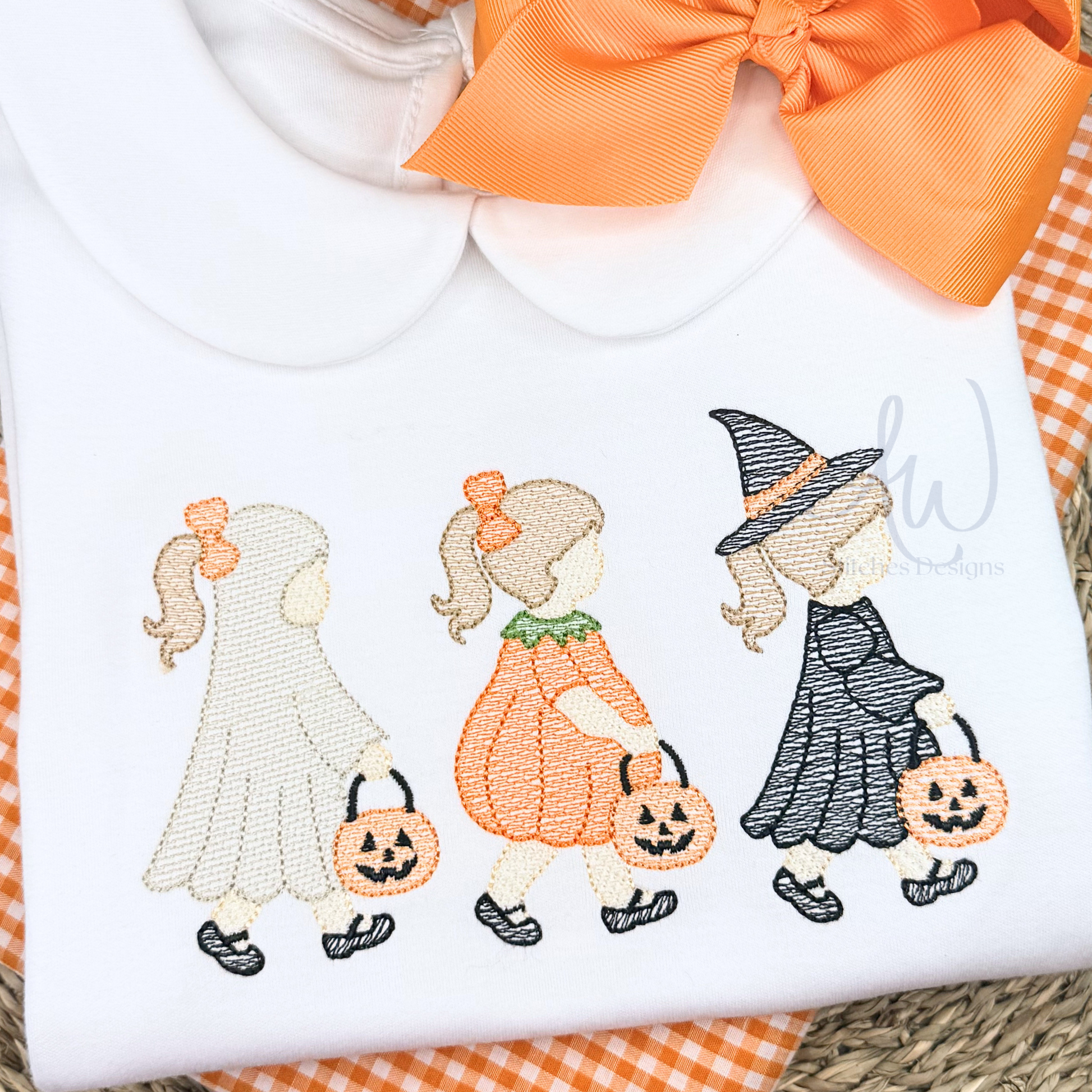 Embroidered design of three children in Halloween costumes on a white fabric background.