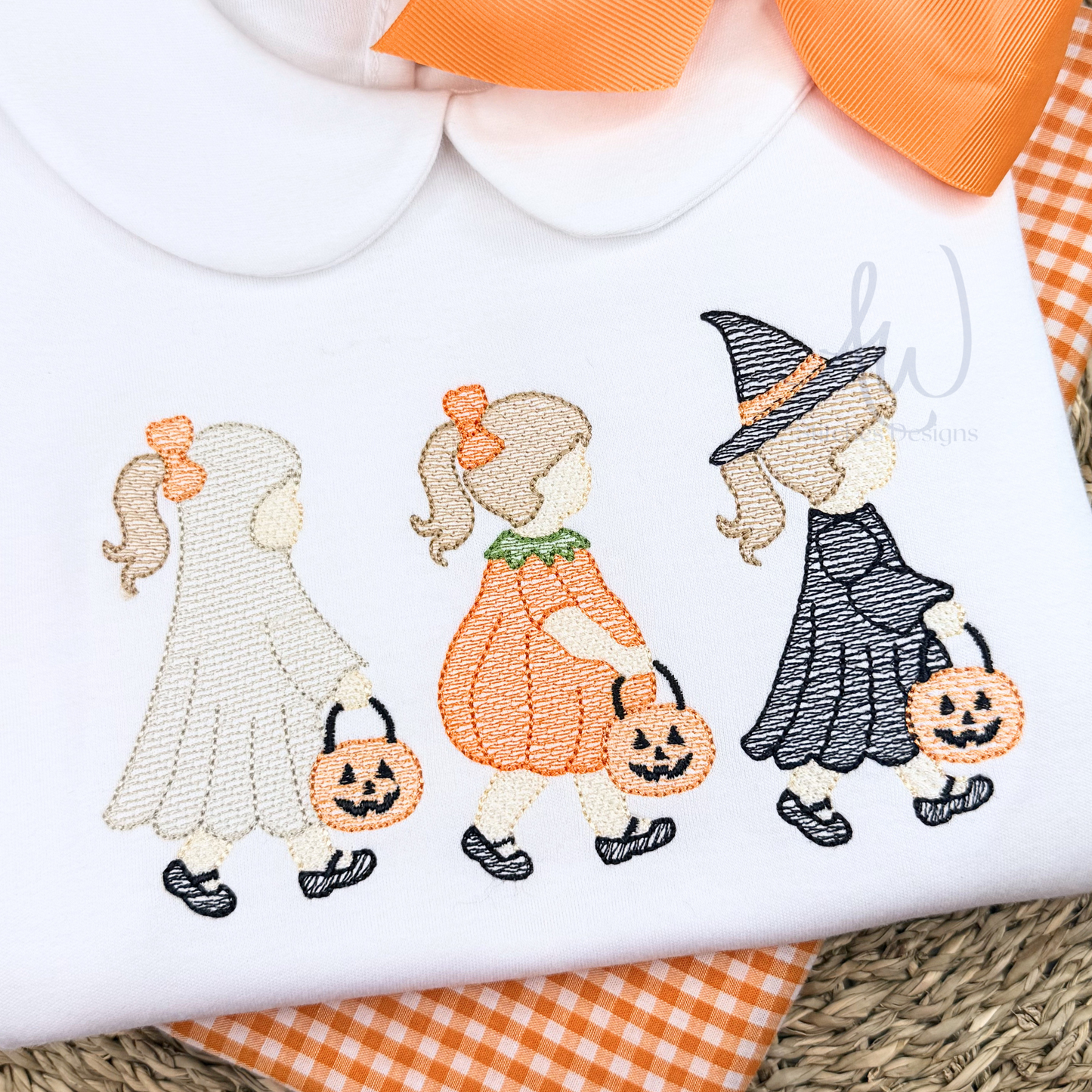 Embroidered design of a ghost, pumpkin girl, and witch on a white fabric background.