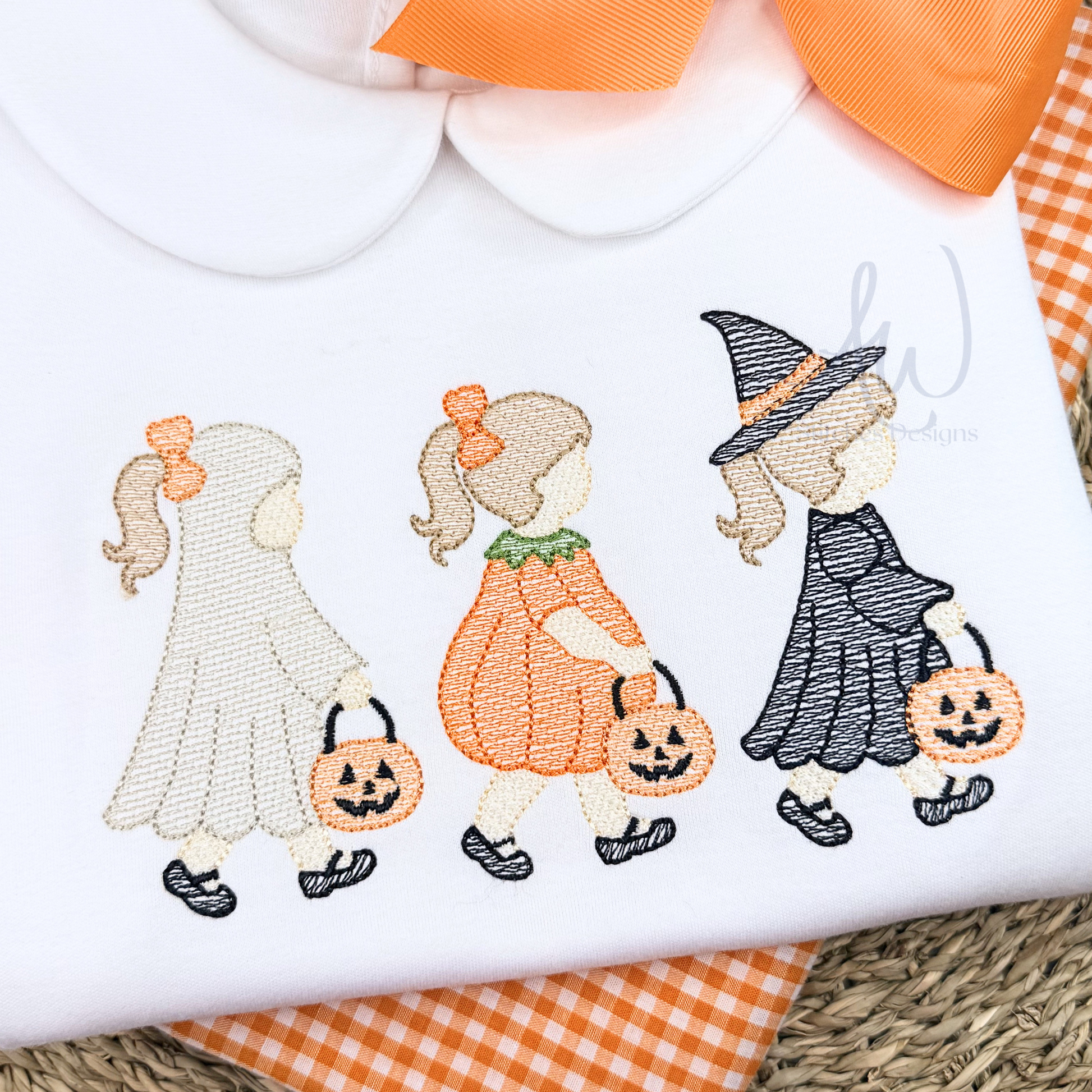 Embroidered design of a ghost, pumpkin girl, and witch on a white fabric background.