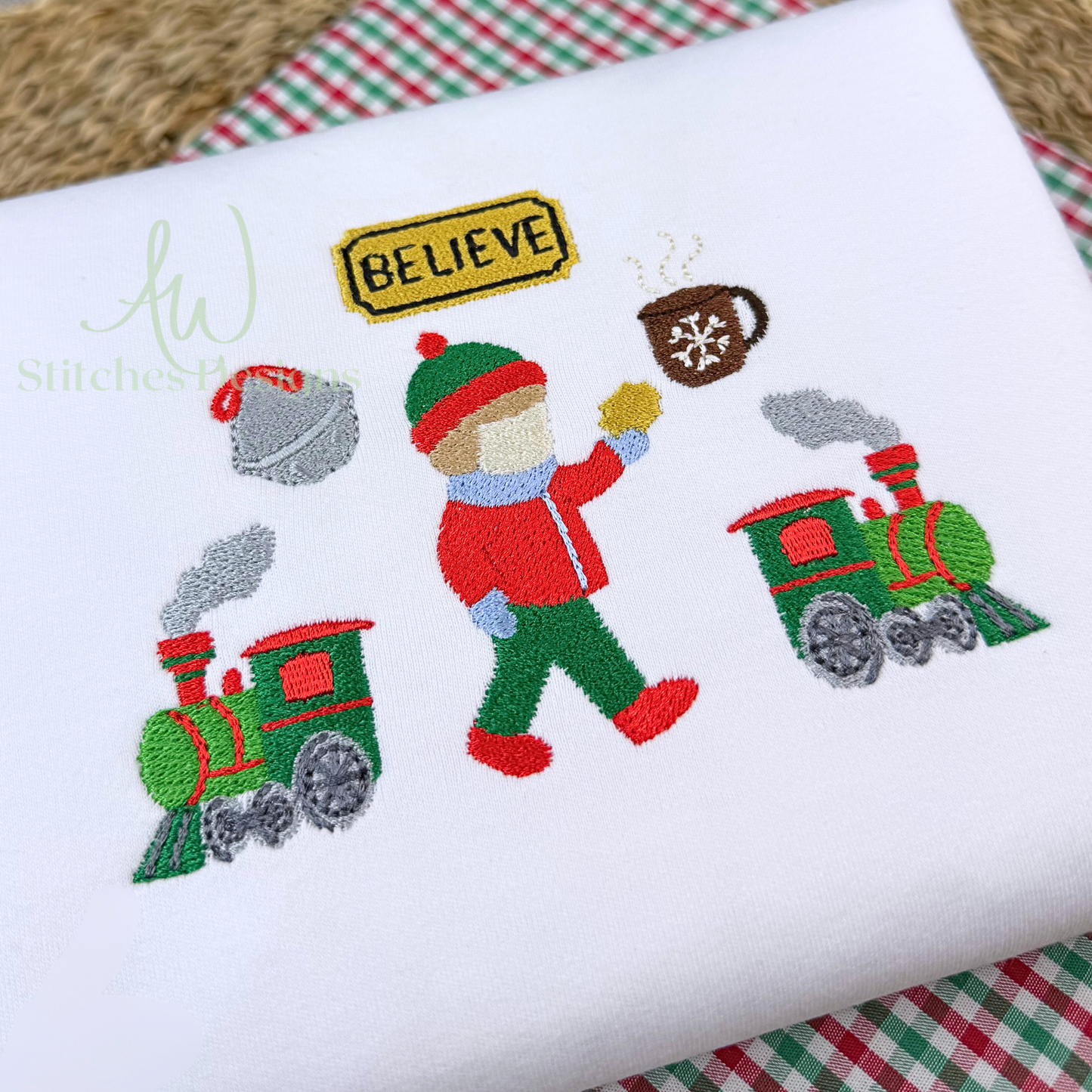 Embroidered design of a child with a train and 'Believe' sign on a white fabric background.