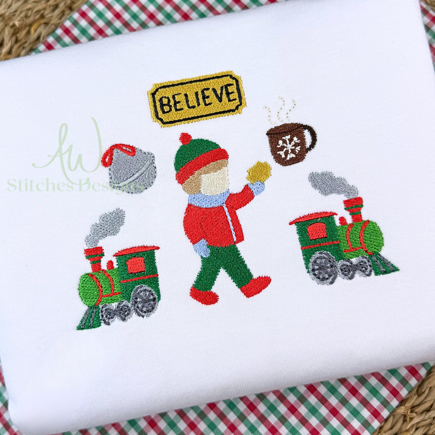 Embroidered design of a person with a train and 'Believe' sign on a white fabric background.