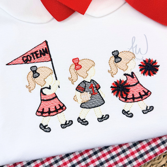 A close-up of a white embroidered baby garment, likely a shirt or bodysuit, featuring three cartoon cheerleader girls walking. One girl holds a pink 'GOTENN' flag, and two others wear red and black pom-poms.